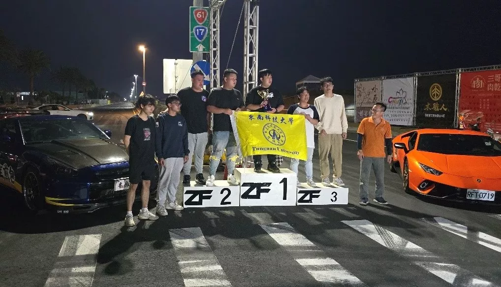 圖1東南科技大學車隊在ZeroFour直線加速賽新能源車組成功奪冠,隊員們手持學校旗幟與獎盃,頒獎台上見證技術與實力的勝利。