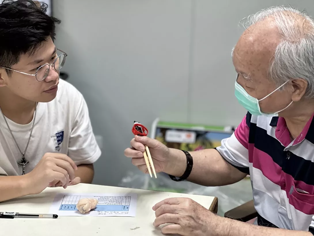 01-學生(左)向標準病人(右)說明為他量身訂做的筷子輔助器,本作品獲113年台灣職能治療學_
