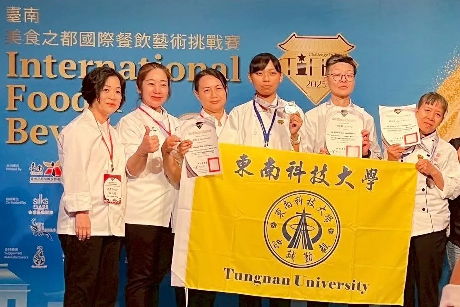 圖一:東南科技大學餐旅管理系師生於國際餐飲藝術競賽中表現優異,共同舉起校旗與獎狀,象徵榮耀與團隊合作精神。
